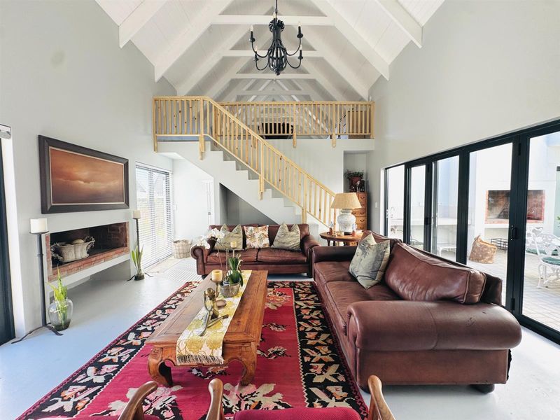 Spacious open-plan living area featuring a vaulted ceiling with exposed beams, a built-in fireplace, and a mezzanine level with wooden balustrades.