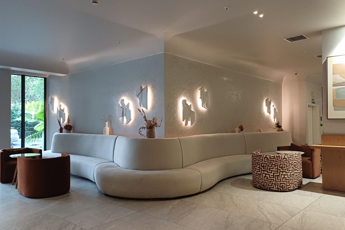 A modern, well-lit lounge area featuring stone flooring, integrated wall sconces, and a curved built-in seating arrangement in a contemporary interior space.
