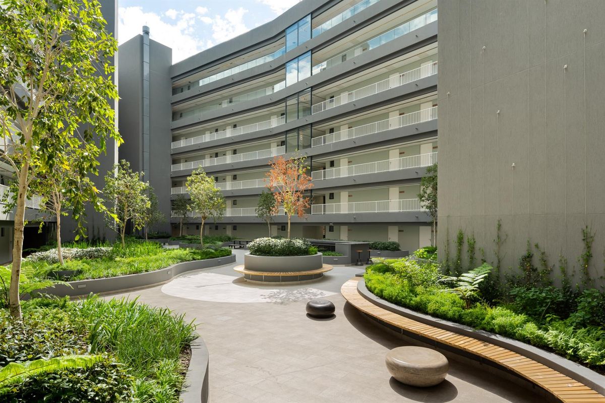 A well-maintained central courtyard featuring landscaped gardens, paved walkways, and built-in seating, surrounded by a modern multi-story residential building with private balconies.