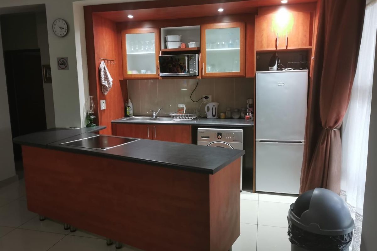 Compact kitchen featuring wood-finish cabinetry, a central island with a built-in cooktop, tiled flooring, and integrated appliance space.