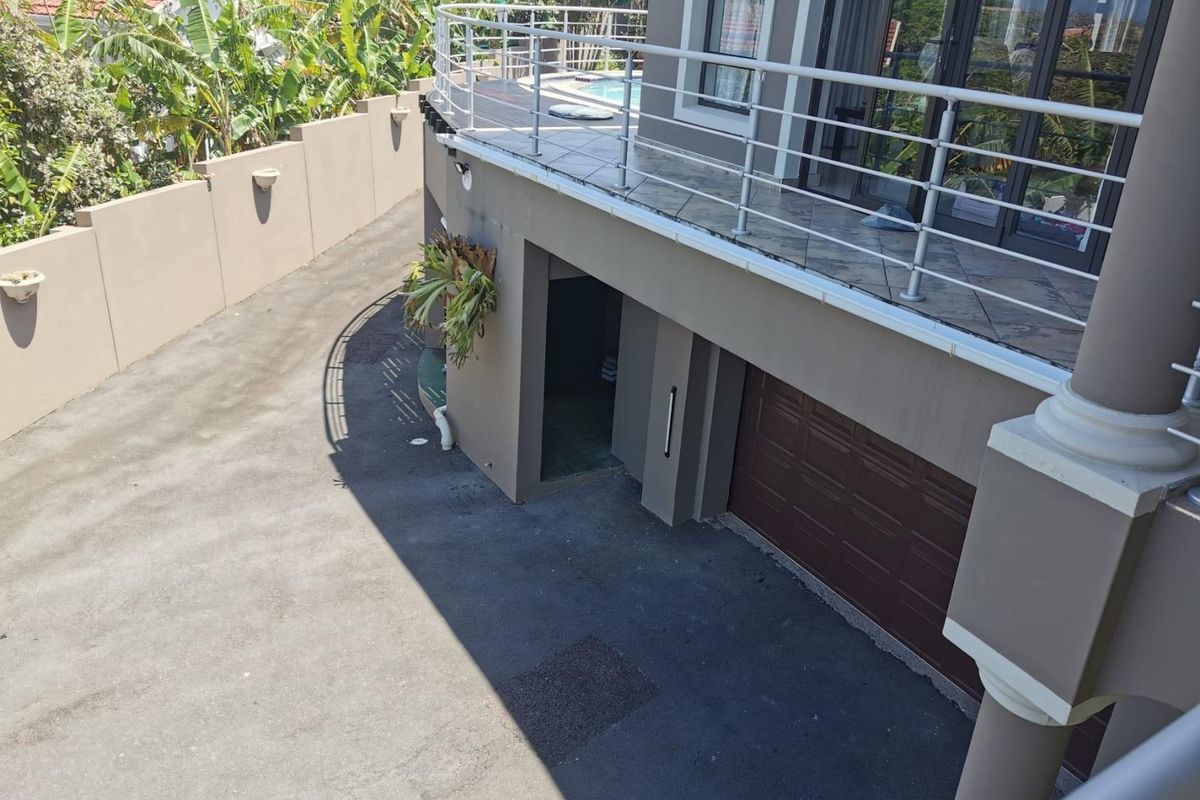 Elevated view of the property exterior featuring a paved driveway, a lower-level garage, and an upper-level balcony with metal railings.