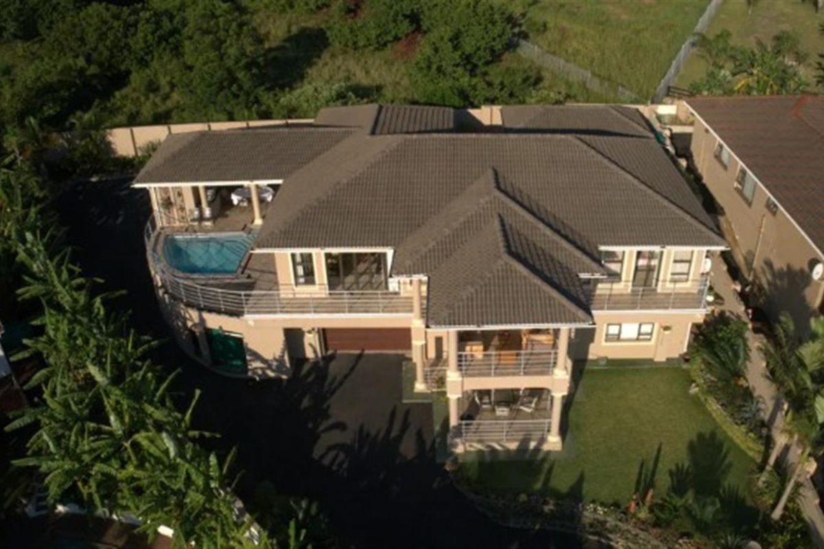 Aerial view of a multi-level residential property featuring a tiled roof, swimming pool, covered balconies, and a paved driveway.