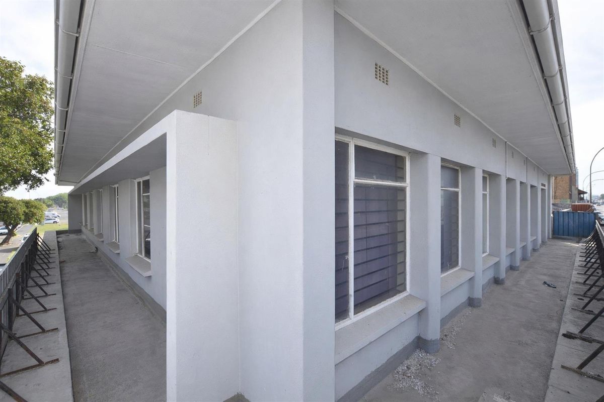 Exterior view of the commercial building featuring a concrete walkway, multiple louvre windows, and a covered eave structure.