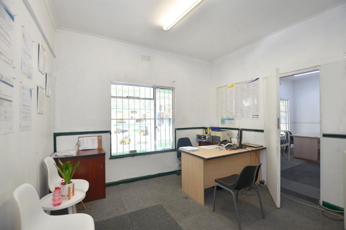 A functional commercial office space featuring carpeted flooring, security bars on the window, and standard fluorescent lighting.
