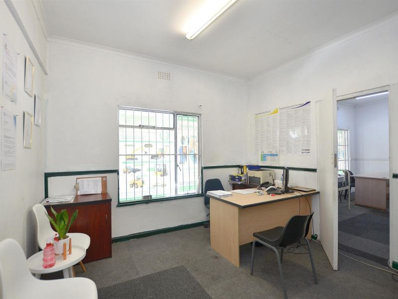 A functional commercial office space featuring carpeted flooring, security bars on the window, and standard fluorescent lighting.