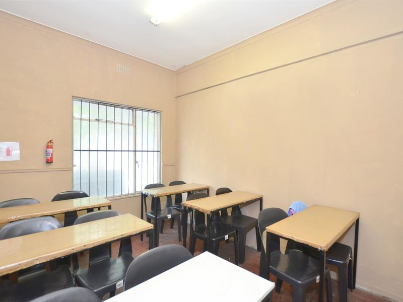 A functional office or classroom space featuring security bars on the window and basic wall-mounted fire safety equipment.