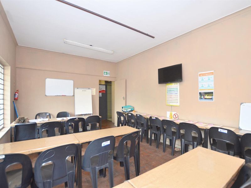 A functional commercial office or training room featuring tiled flooring, security window bars, and overhead fluorescent lighting, suitable for various business or educational purposes.