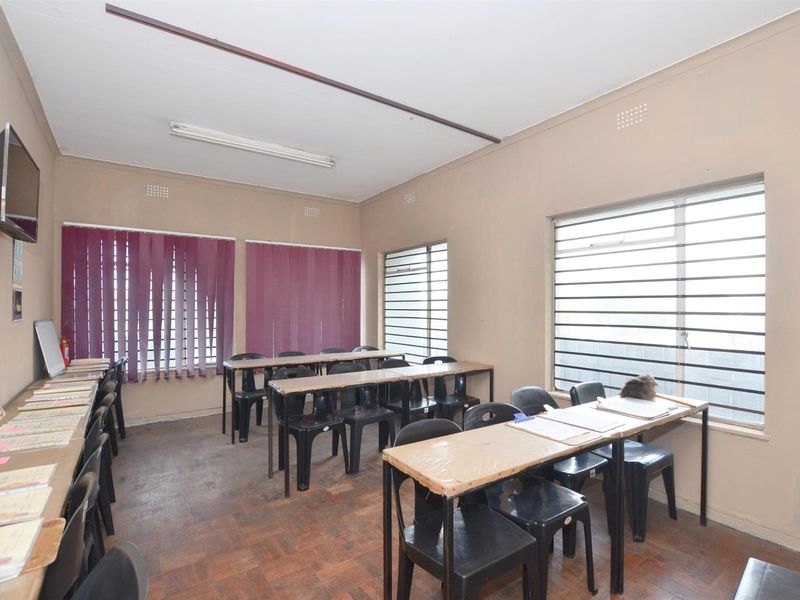 A functional office or classroom space featuring parquet flooring, multiple windows with blinds, and basic electrical infrastructure.