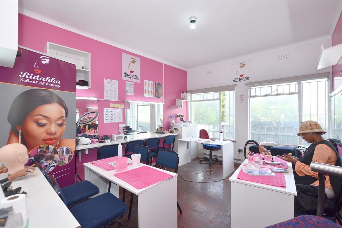A functional commercial studio space featuring parquet flooring, built-in vanity mirrors, and large windows with security bars, suitable for beauty or professional services.
