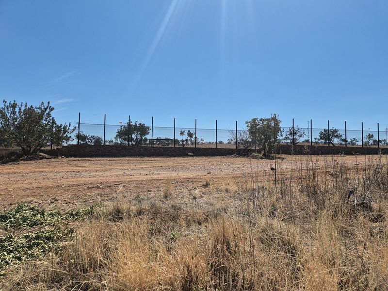 A view of the vacant residential land featuring a stone retaining wall and perimeter wire mesh fencing with electric security wires.