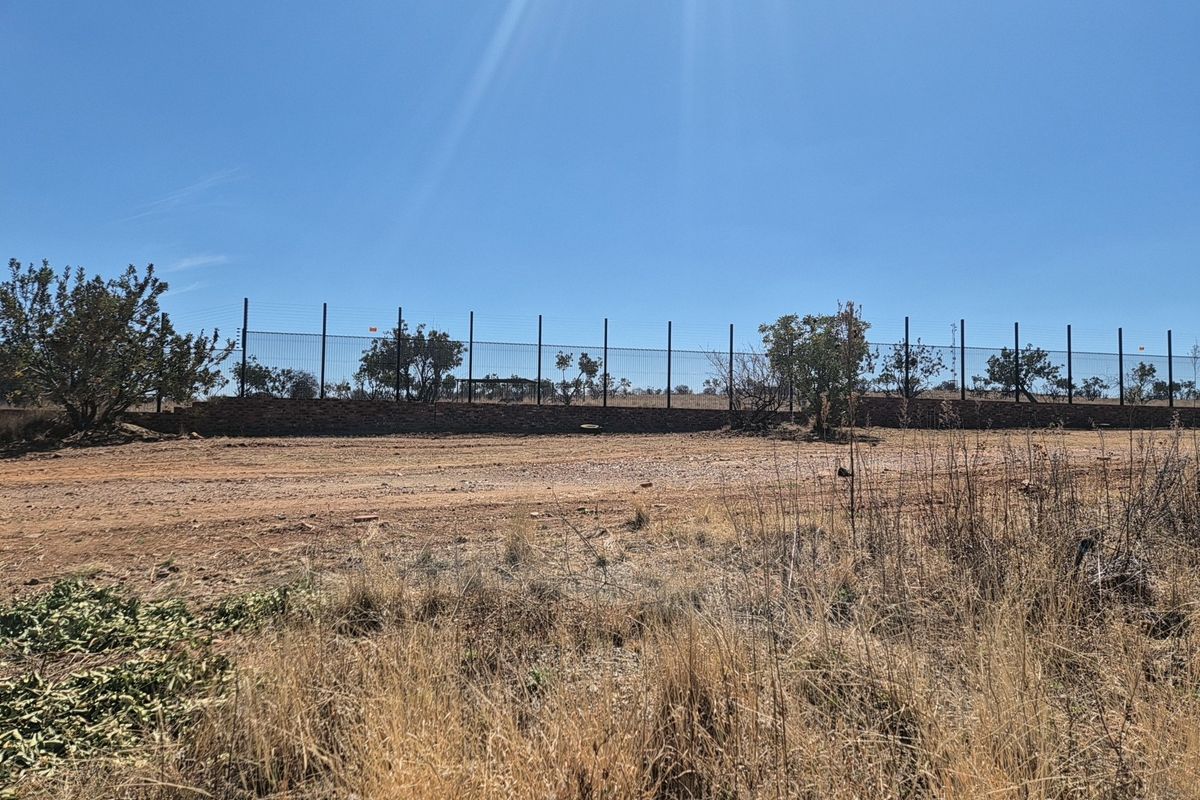 A view of the vacant residential land featuring a stone retaining wall and perimeter wire mesh fencing with electric security wires.