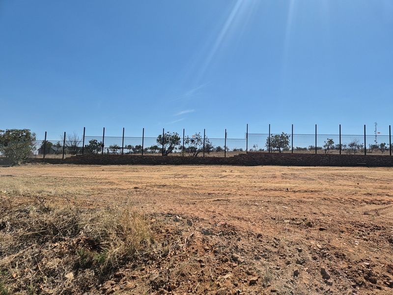 A vacant residential plot featuring a secure brick boundary wall topped with electric fencing, ready for development.