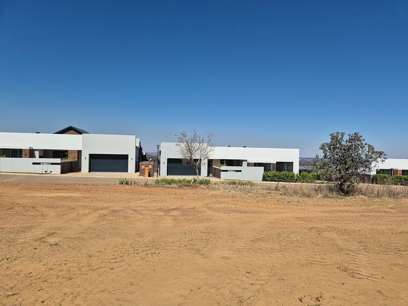 A view of modern residential properties with garages, situated on a vacant plot of land with clear blue sky.