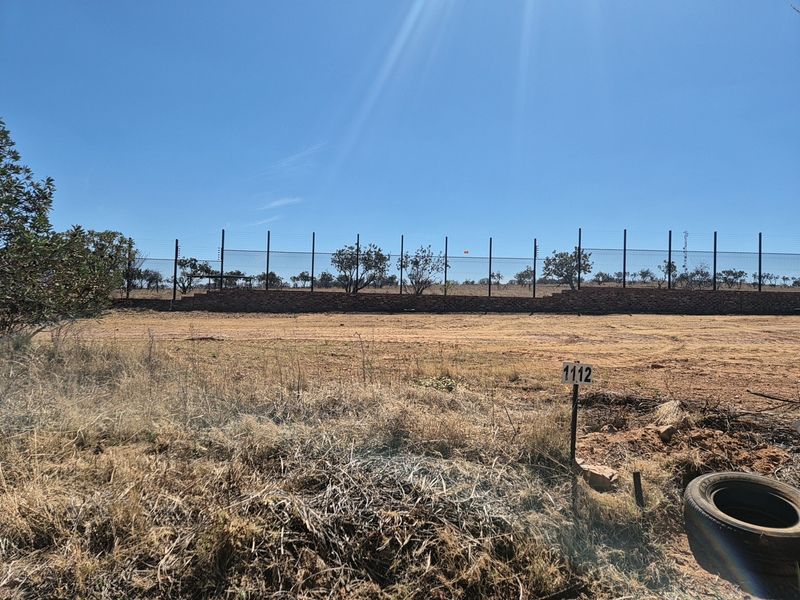 A vacant residential plot featuring a perimeter wall with electric fencing and a clear lot marker, ready for development.