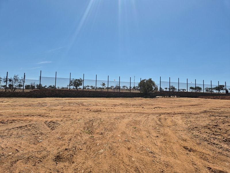 A vacant residential plot featuring a secure perimeter with brick retaining walls and installed electric fencing.