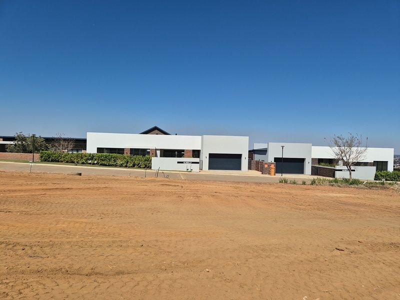 A view of modern residential properties with garages and paved driveways, situated adjacent to an undeveloped plot of land.