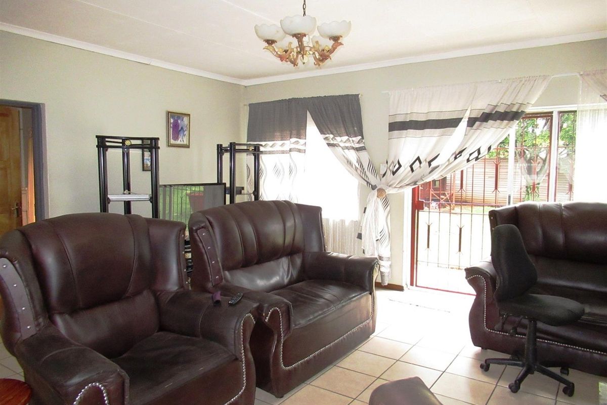 A living room featuring tiled flooring, a central chandelier, and access to an outdoor area through a security-gated door.