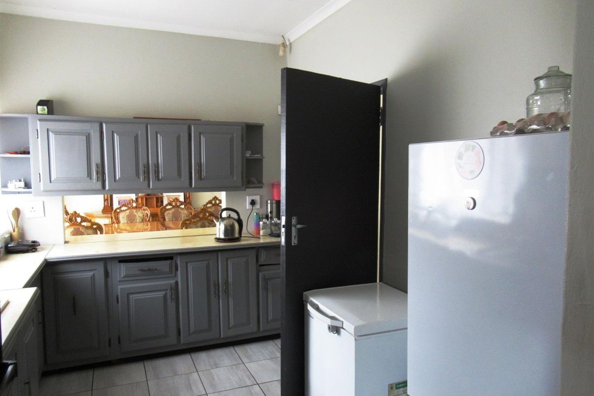 A functional kitchen area featuring grey cabinetry, tiled flooring, and a mirrored backsplash, providing ample storage and workspace.
