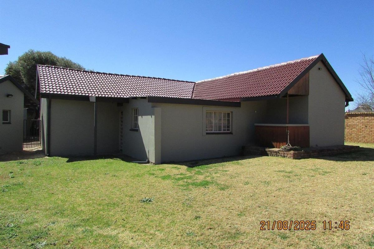 Rear view of the house featuring a tiled roof, brick-built outdoor feature, and a spacious backyard area.