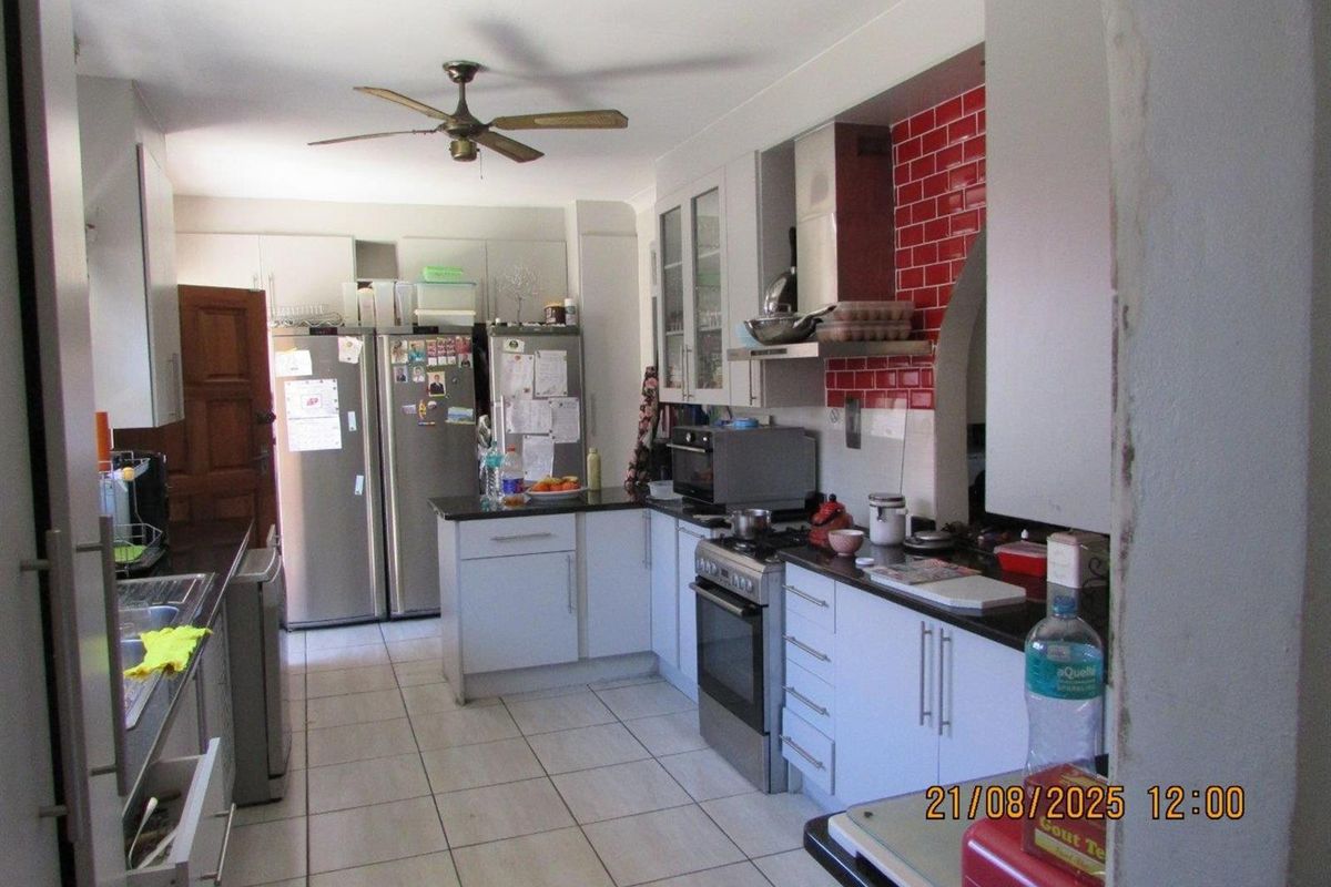 Functional kitchen featuring white cabinetry, dark countertops, a red tiled backsplash, and a ceiling fan, providing a practical workspace for daily cooking.