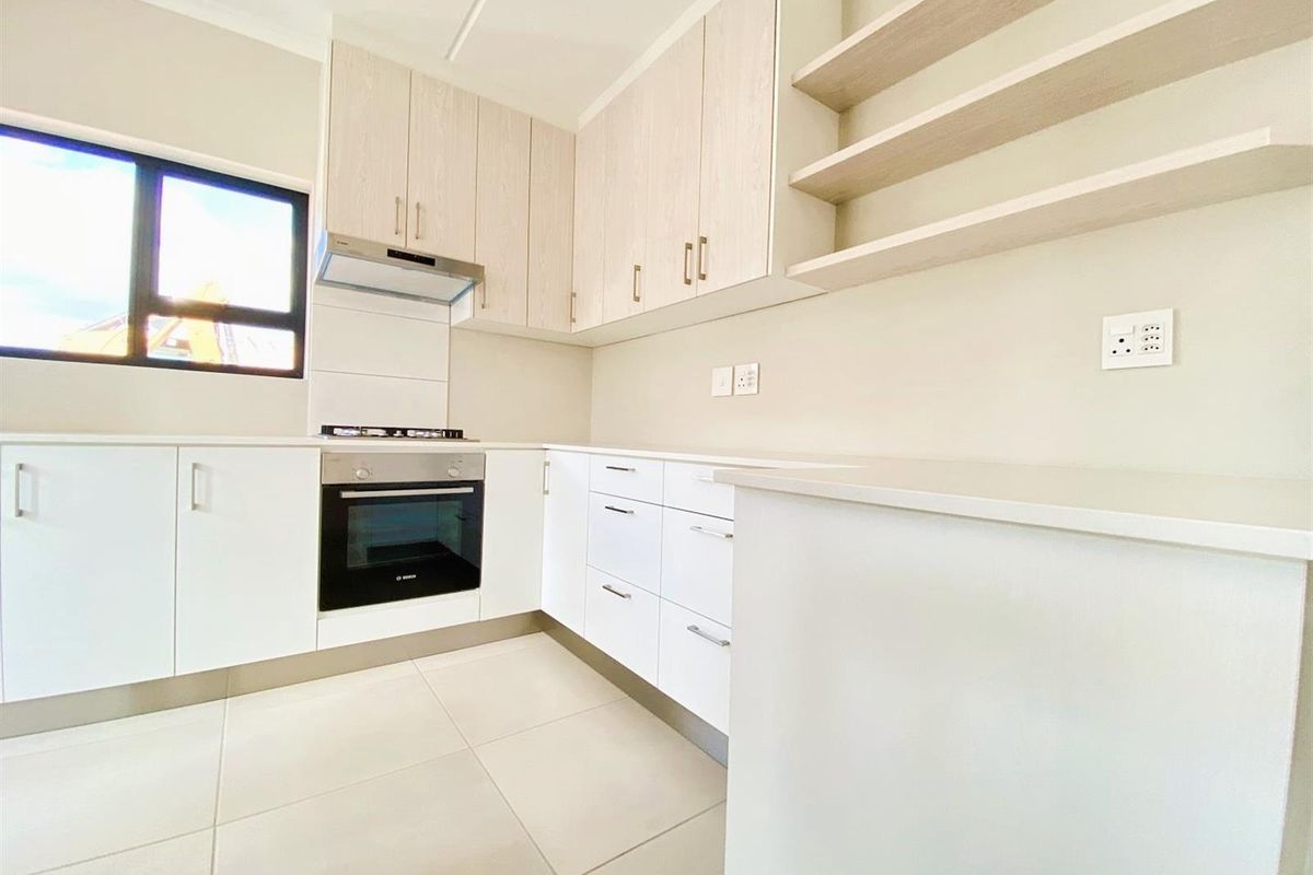 Modern kitchen featuring light-toned cabinetry, built-in oven, gas hob, extractor fan, and tiled flooring in a clean, minimalist design.