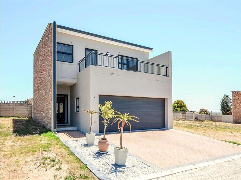 Modern double-story house featuring a paved driveway, double garage, and an upper-level balcony with metal railings.