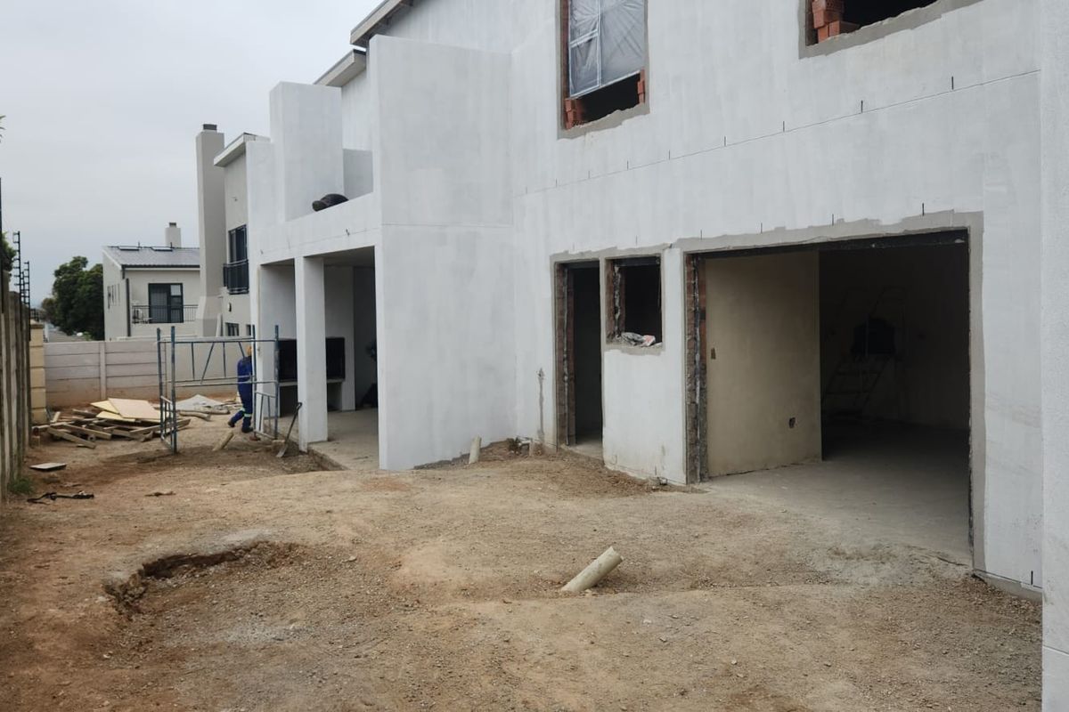 Rear view of a residential property under construction, featuring a plastered facade, covered patio area, and an open garage space with unlandscaped grounds.