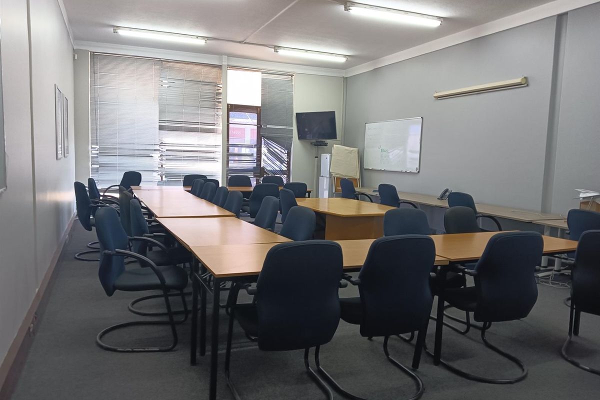 A functional office meeting room featuring fluorescent lighting, wall-mounted whiteboard, and large windows with venetian blinds.