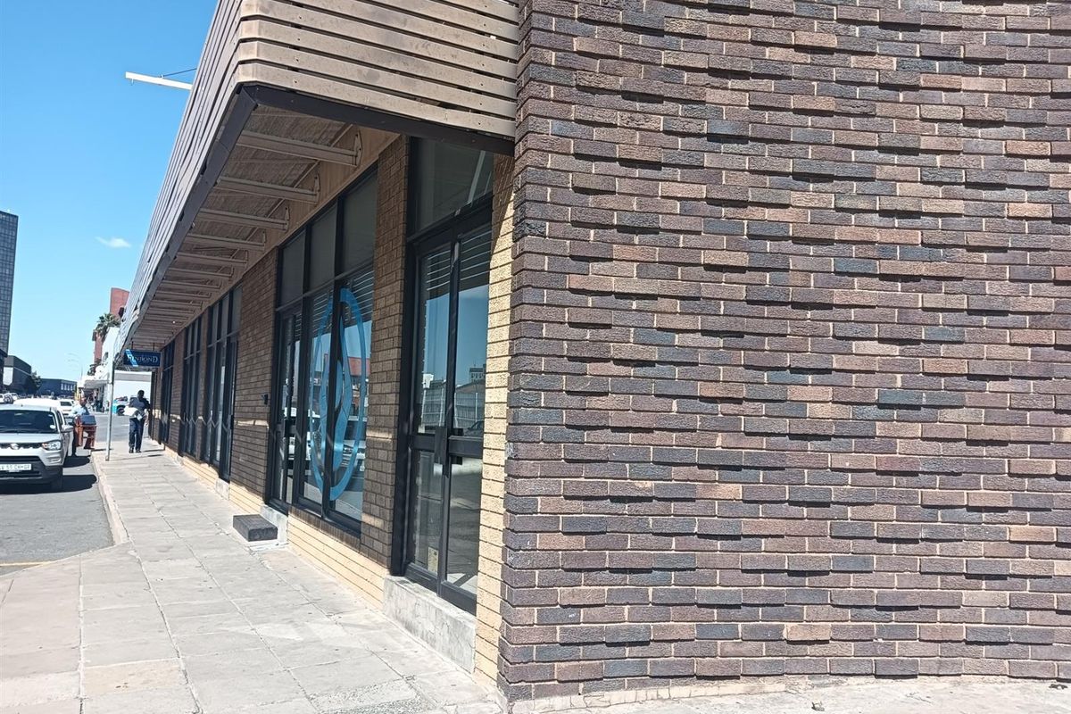 Street-level view of an office building featuring a textured brick facade, large glass storefront windows, and a timber-slat awning over the sidewalk.