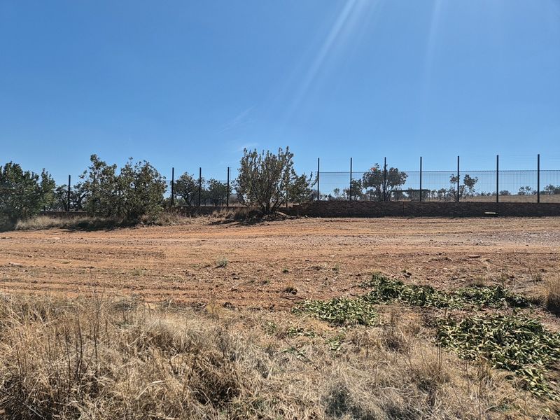 A vacant residential plot featuring a level terrain, perimeter fencing, and a low retaining wall, ready for development.
