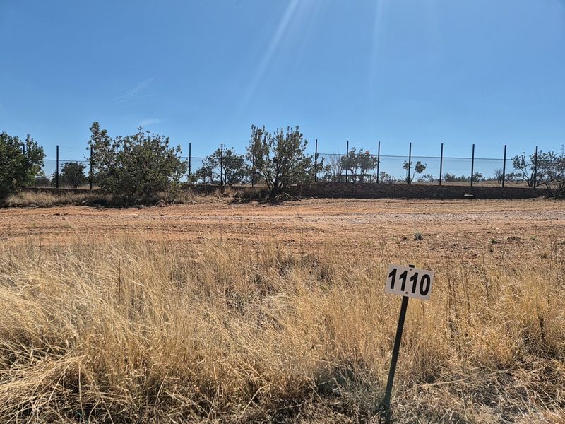 A vacant residential plot featuring dry grass, a boundary wall, and electric fencing, marked with a plot number sign.