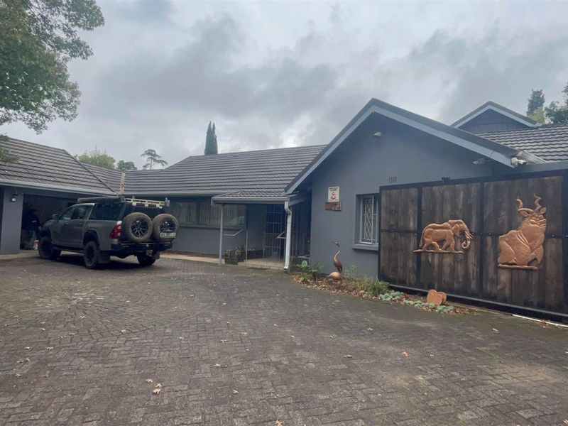 Front elevation of a residential property featuring a paved driveway, double garage, and a large sliding gate with decorative wood carvings.