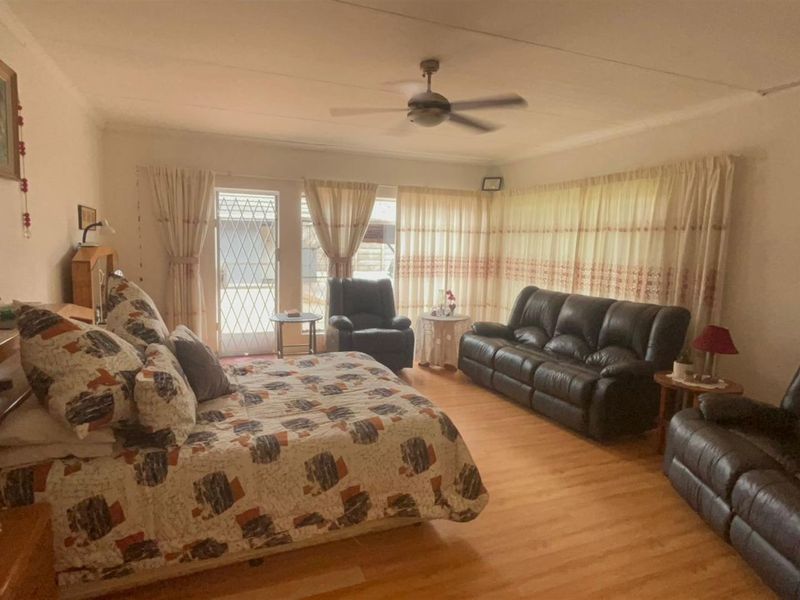 Spacious bedroom featuring laminate flooring, a ceiling fan, and direct access to the exterior through a security gate.
