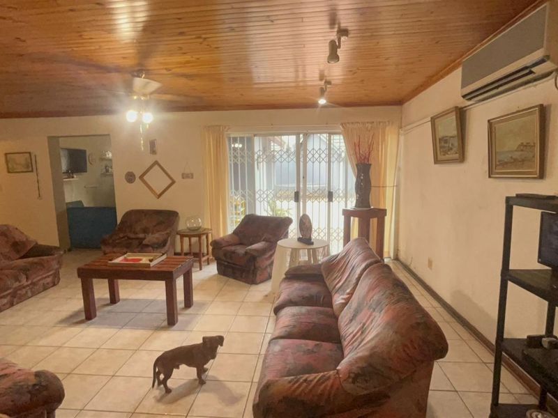 Spacious living room featuring a timber tongue and groove ceiling, ceramic tiled flooring, and direct access to the patio through sliding glass doors.