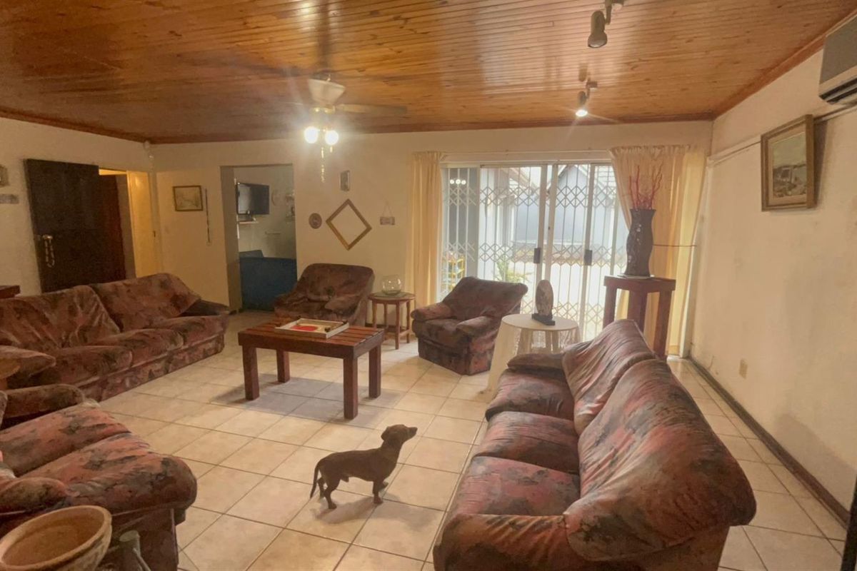 Spacious living room featuring a timber-clad ceiling, tiled flooring, and a sliding glass door with security gate leading to the exterior.