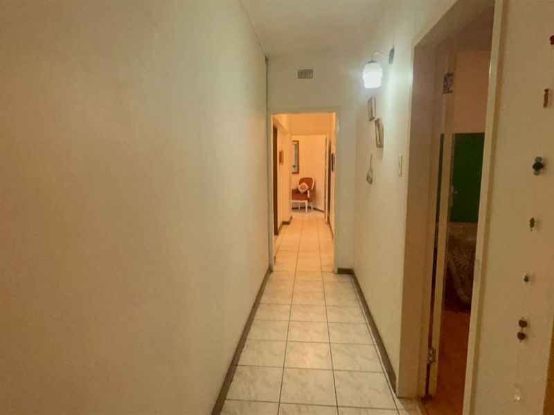 A narrow interior hallway featuring tiled flooring and wall-mounted lighting, providing access to adjacent rooms within the property.