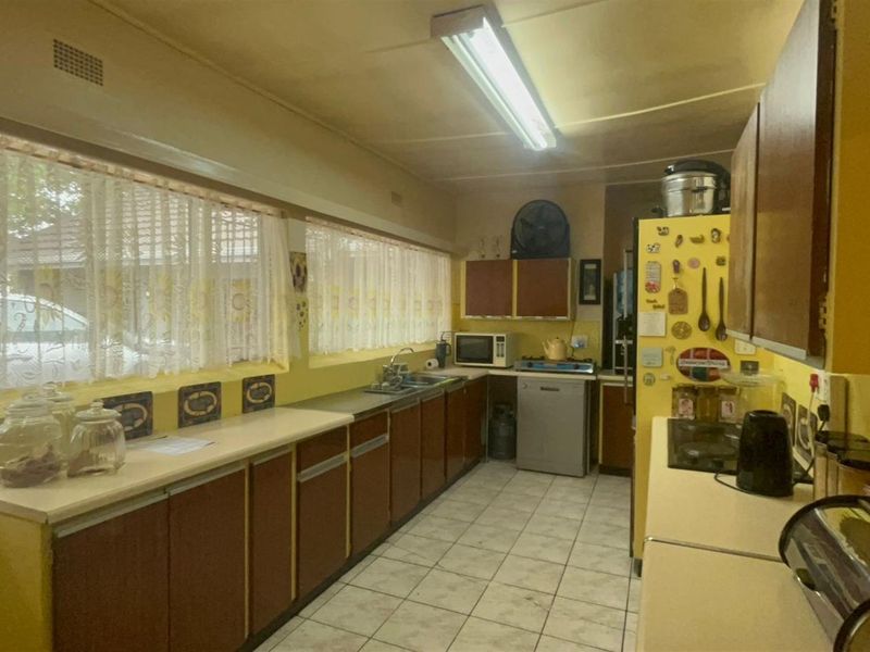 A dated kitchen featuring original cabinetry, laminate countertops, tiled flooring, and functional layout, offering significant potential for a modern renovation.