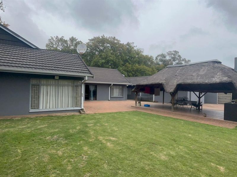 Spacious rear garden featuring a paved patio area and a traditional thatched lapa with a built-in braai, perfect for outdoor entertaining.