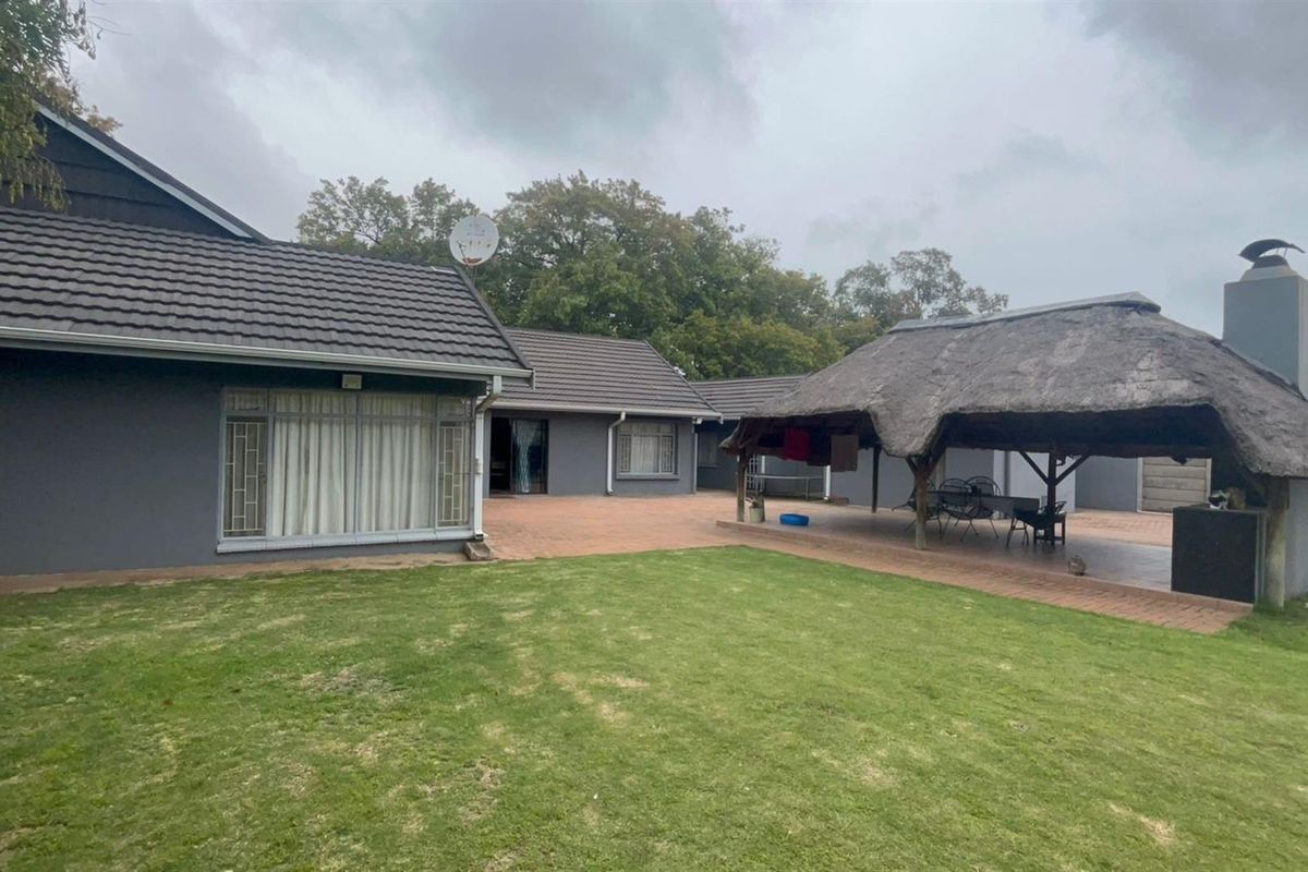 Spacious rear garden featuring a paved patio area and a traditional thatched lapa with a built-in braai, perfect for outdoor entertaining.
