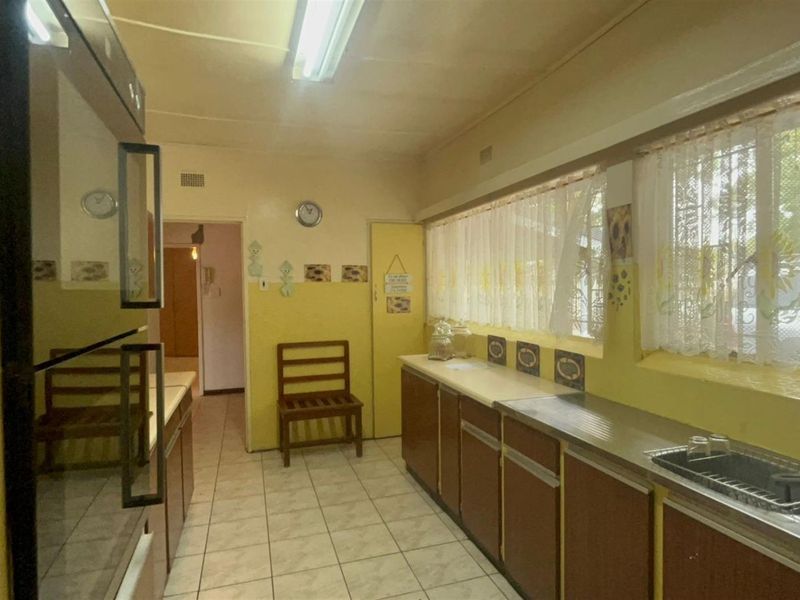 A functional kitchen featuring dated cabinetry, tiled flooring, a built-in oven, and a stainless steel sink with ample natural light.