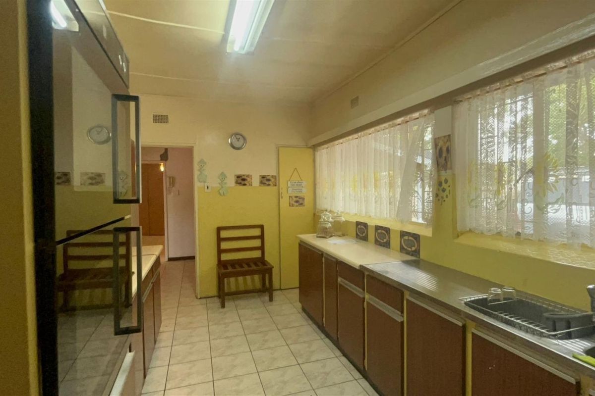 A functional kitchen featuring dated cabinetry, tiled flooring, a built-in oven, and a stainless steel sink with ample natural light.