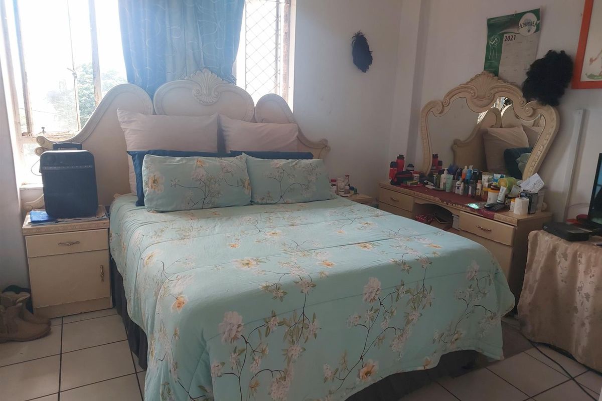 A bedroom featuring tiled flooring and a window with security bars, providing natural light.