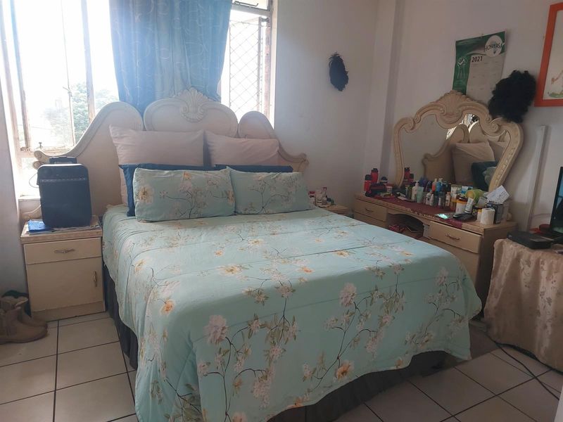 A bedroom featuring tiled flooring and a window with security bars, providing natural light.