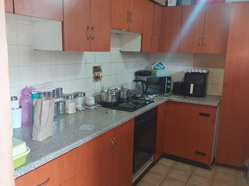 A functional kitchen featuring wood-tone cabinetry, laminate countertops, a built-in oven, and a ceramic hob, with tiled flooring throughout.