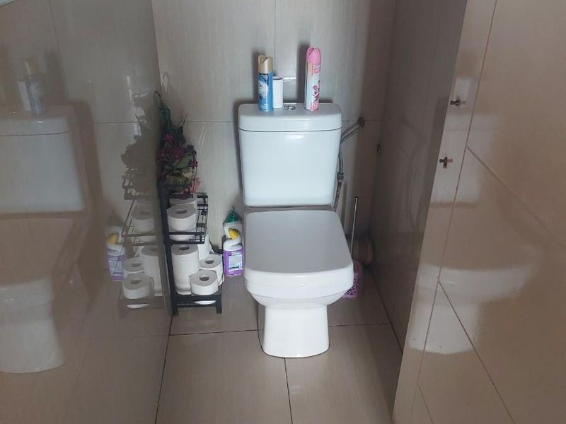 A compact bathroom featuring floor-to-ceiling wall tiles with a decorative mosaic border and a modern white toilet suite.