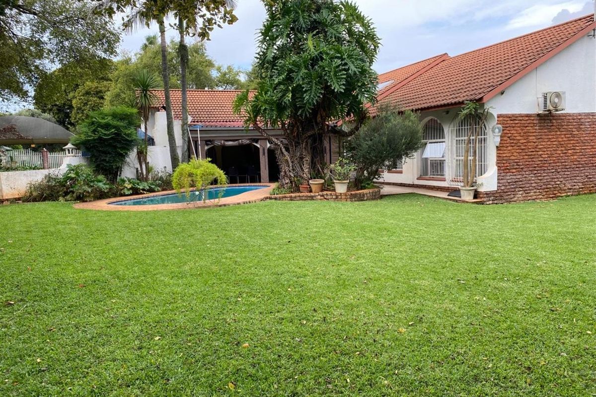 Spacious rear garden featuring a swimming pool, established trees, and a house exterior with terracotta roof tiles and brick detailing.