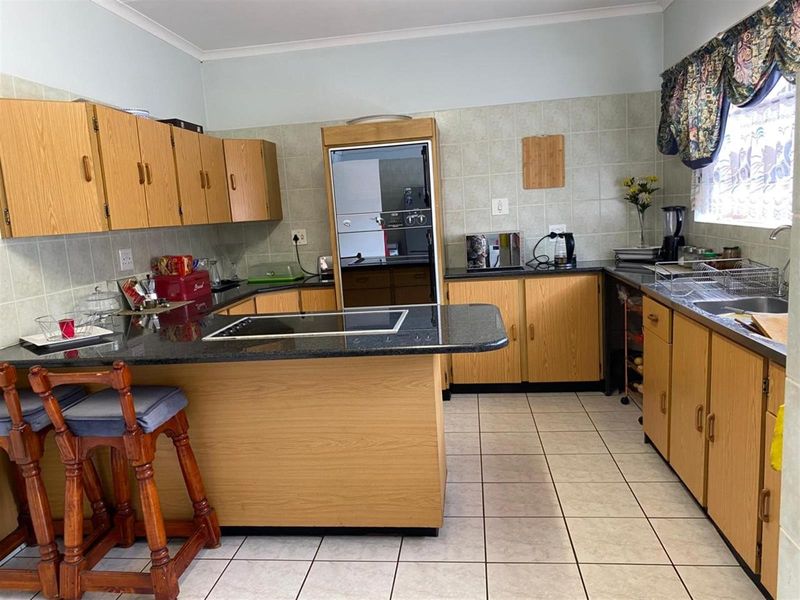 A functional kitchen featuring wood-finish cabinetry, granite countertops, a built-in oven, and an electric hob with tiled flooring and backsplash.