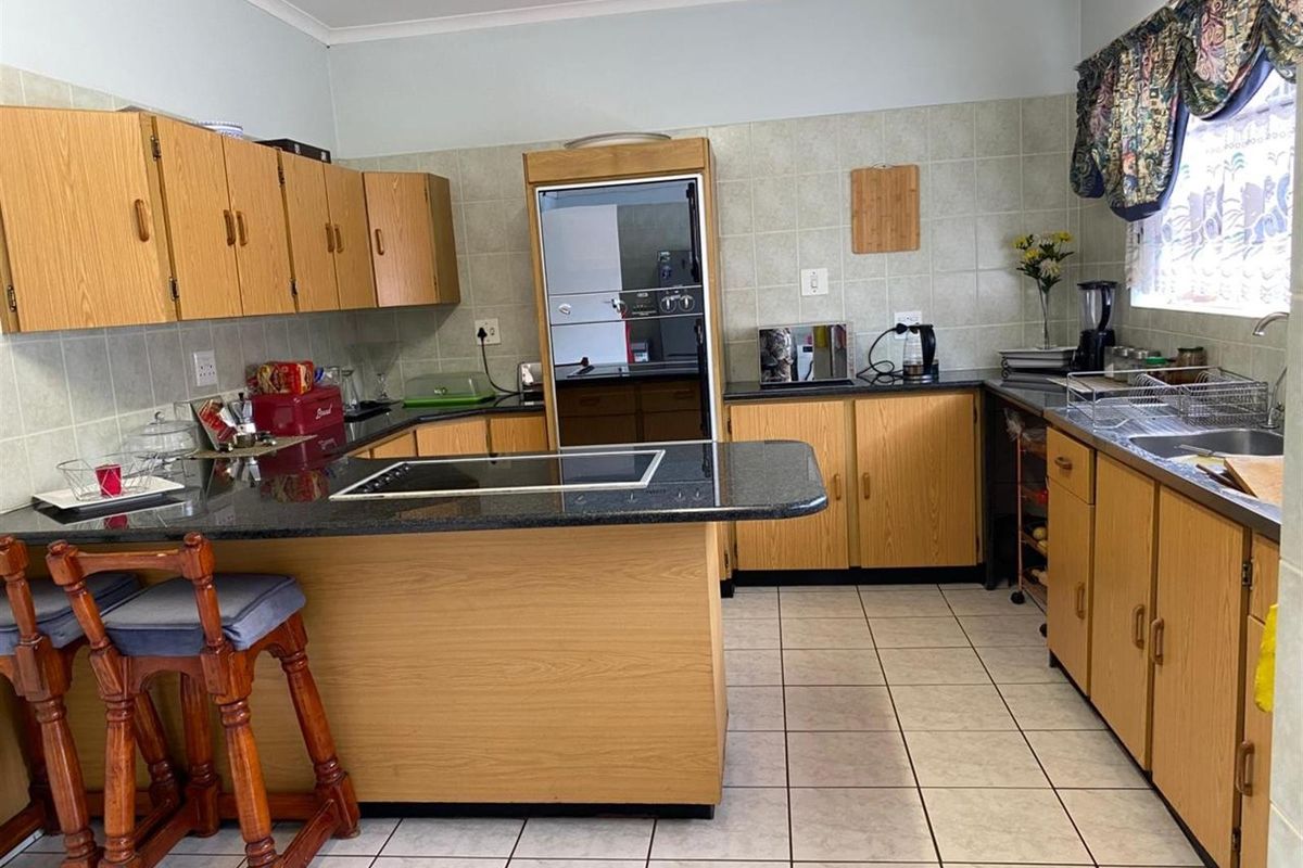 A functional kitchen featuring wood-finish cabinetry, granite countertops, a built-in oven, and an electric hob with tiled flooring and backsplash.