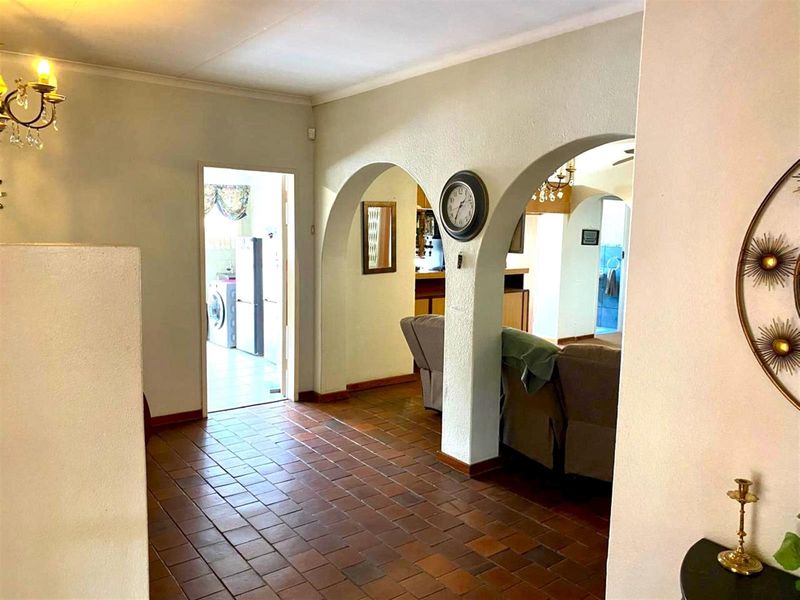 A spacious hallway featuring traditional terracotta floor tiles and distinctive arched architectural details connecting to adjacent living and utility areas.
