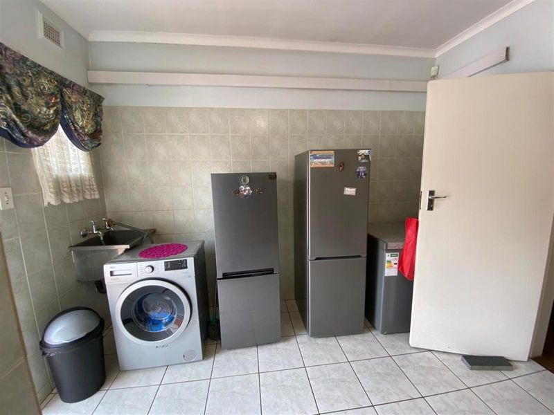 A functional laundry area featuring tiled walls and flooring, equipped with a stainless steel utility sink and dedicated plumbing connections for appliances.